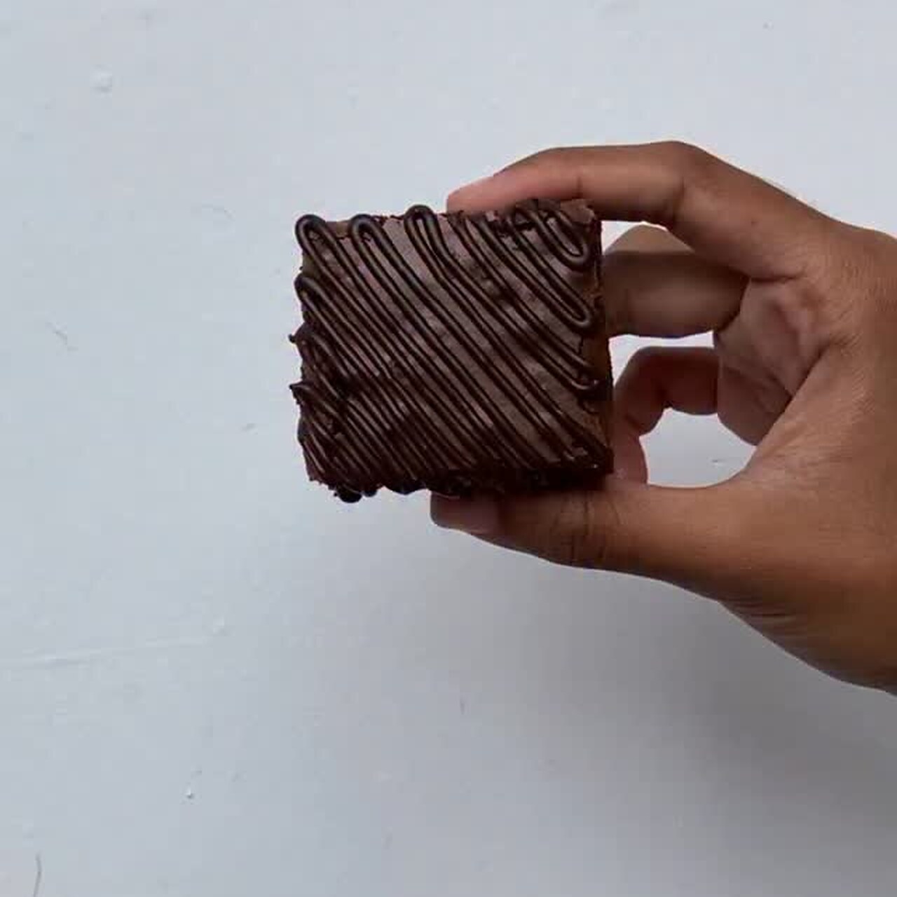 A hand holding a chocolate-drizzled brownie square